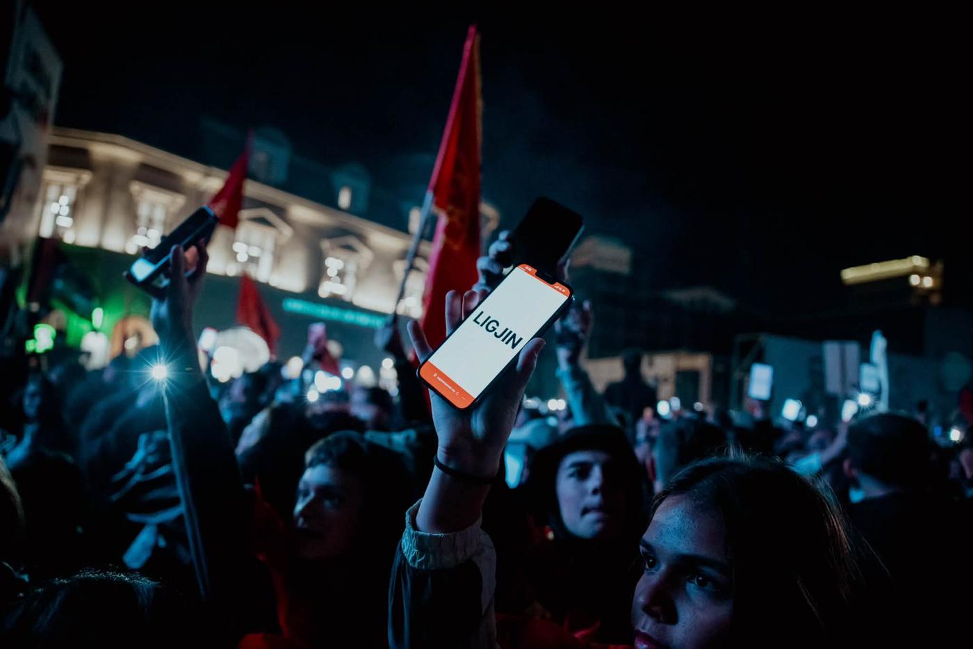 A raised phone showing the word LIGJIN in a protest crowd